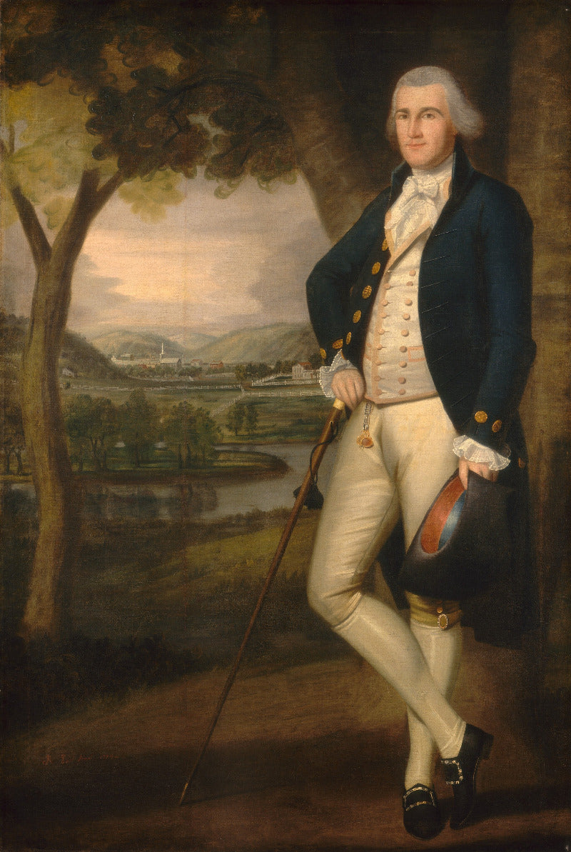 A formal portrait painting of a man in historical attire, wearing a dark blue coat, white waistcoat and breeches, with a white powdered wig, standing indoors near a tree and holding a hat and cane. The background shows a painted landscape with trees, water, and distant hills.